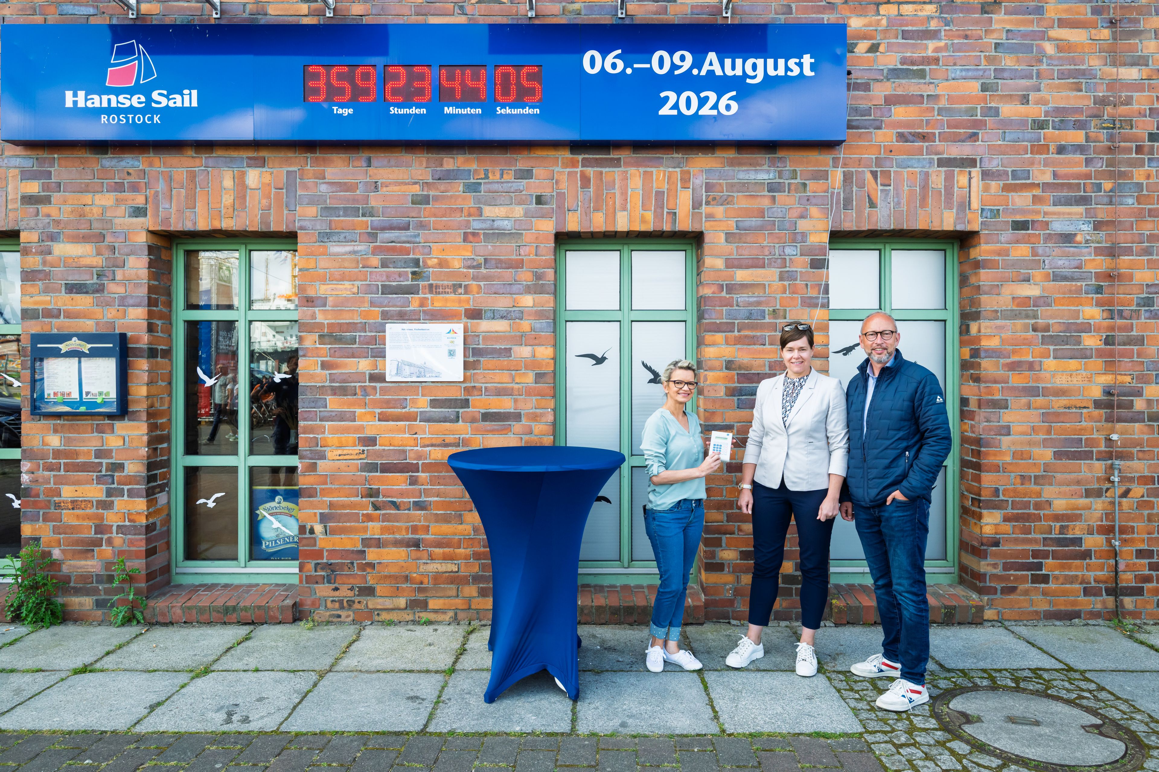 Bettina Fust, Eva-Marie Kröger und Matthias Fromm drücken den Knopf der Countdown-Uhr der Hanse Sail
