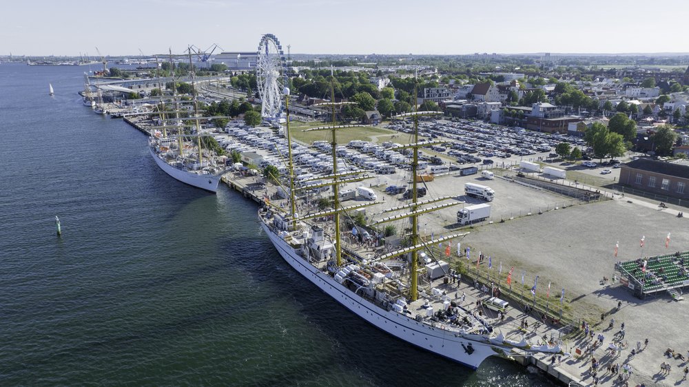 Luftaufnahme von zwei Großsegelschiffen an Kai Kante. Viele Fahrzeuge und Riesenrad im Hintergrund 