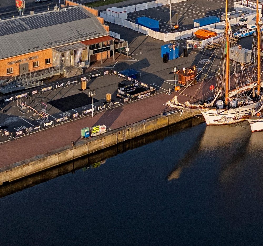 Luftaufnahme von Schiffen die an Kai kante liegen. Auf dem Größten Schiff ist die Aufschrift Koi und neben dem Schiff ist ein Zirkuszelt aufgebaut