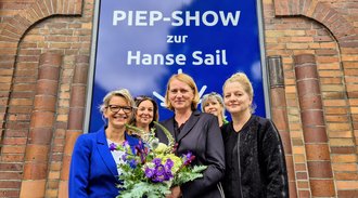 Bettina Fust, Chefin der Hanse Sail, überreicht Blume vor dem Schaufenster des Modehaus Nikolaus in der Innenstadt Rostocks
