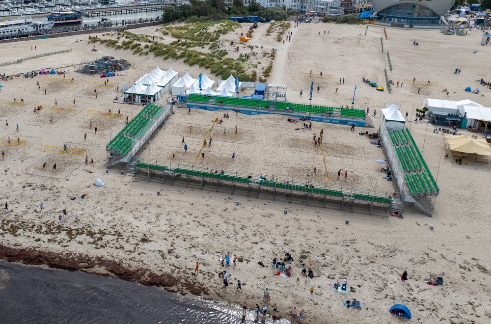 Luftaufnahme Warnemünde Strand mit Volleyball Felder in Arena. Im Hintergrund Warnemünde mit Yachthafen und Kreuzfahrtschiff 